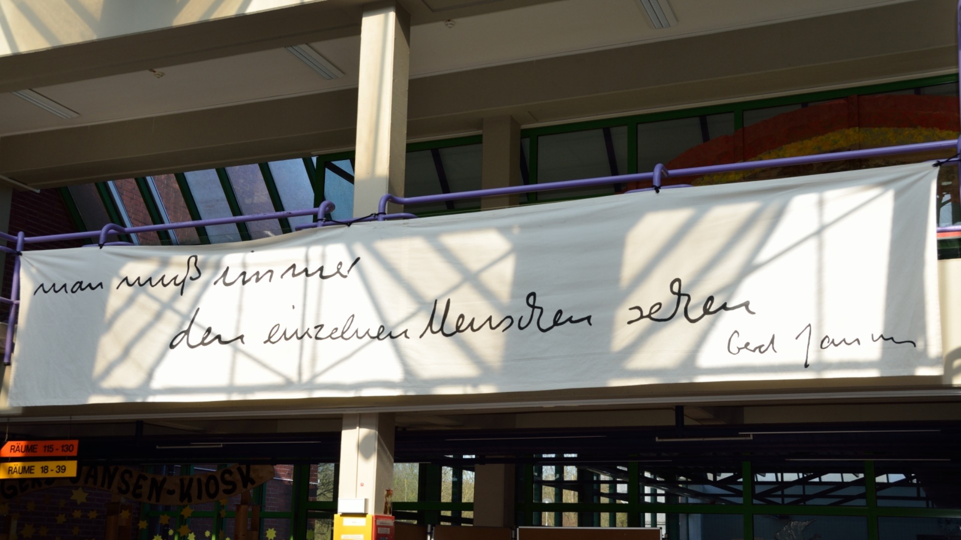 Auf einem weißen Banner, das vor dem Schuleingang von oben hängt steht in schwarzer Schreibschrift: "Man muss immer den Menschen sehen. Gerd Jansen"
