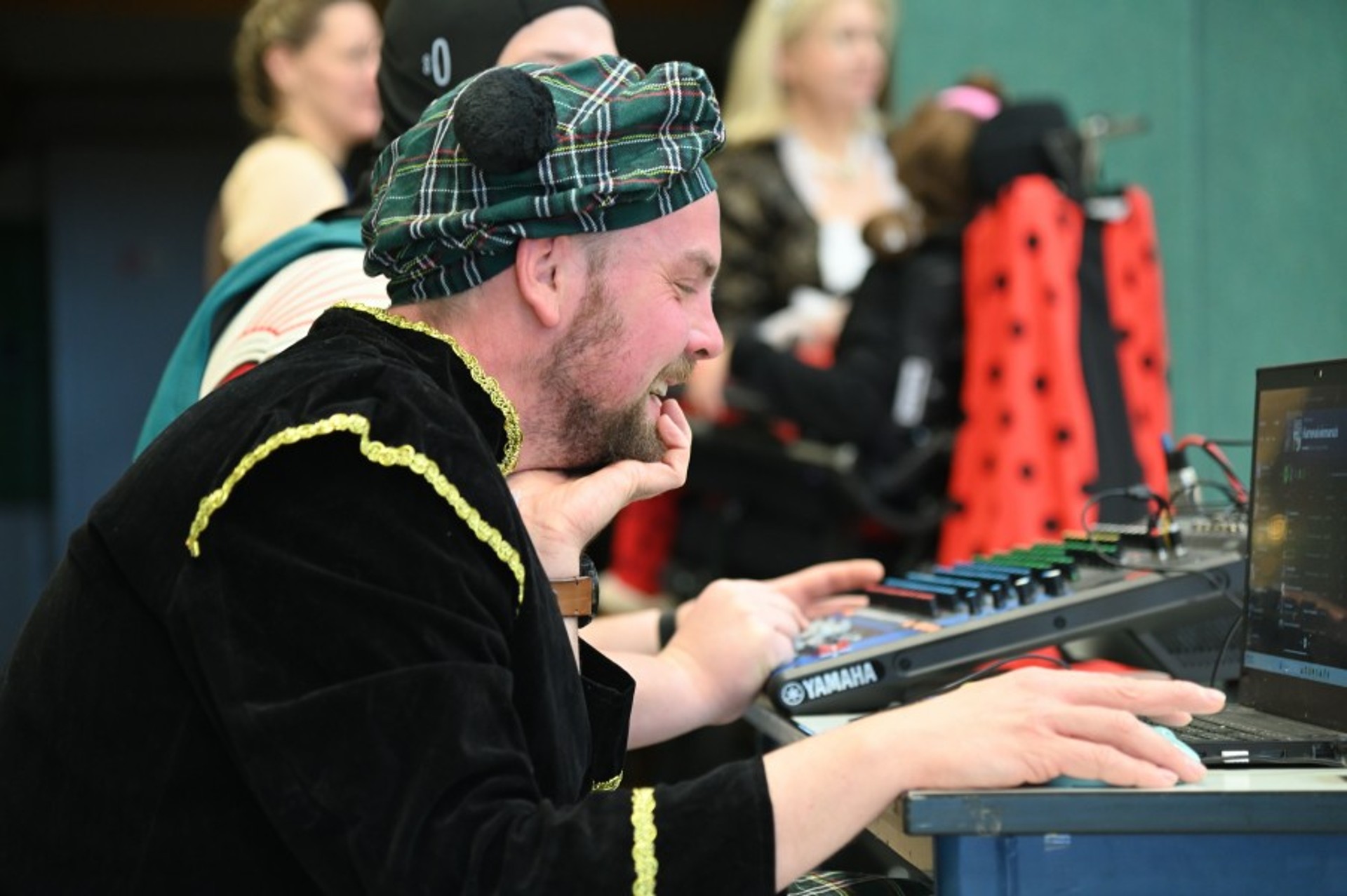 Ein als Schotte verkleideter Mann sitz an einem Tisch, vor ihm ein Notebook, neben ihm ein Mischpult. Er hat ein breites Grinsen im Gesicht.