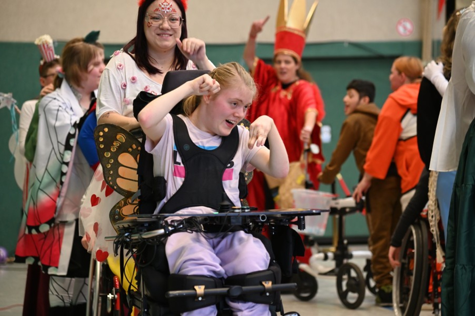 Verkleidete Menschen mit und ohne Rollstuhl oder Gehhilfen ziehen in einer Polonaise durch die Turnhalle.