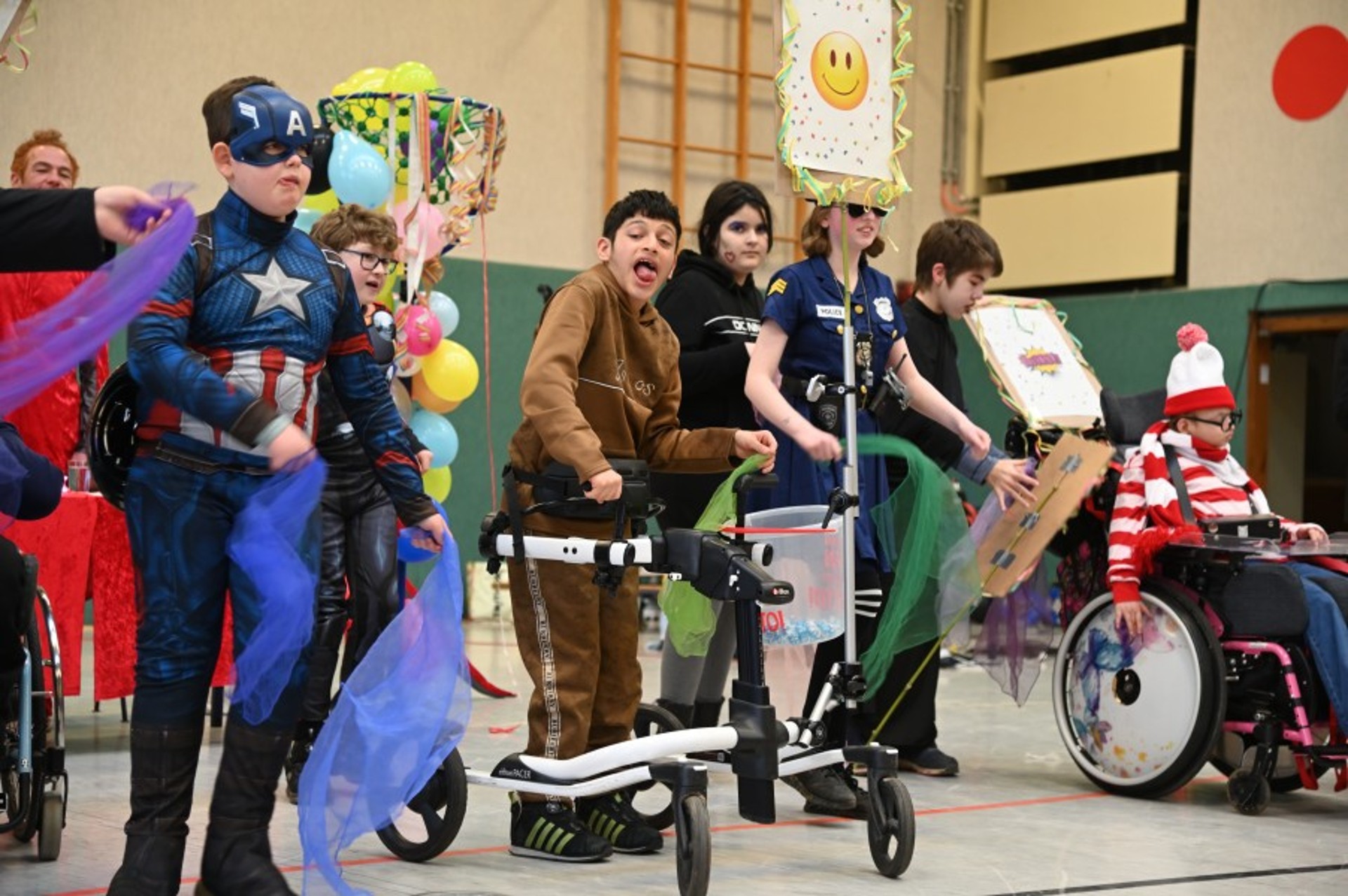 In einer Turnhalle tanzen verkleidete Kinder und Jugendliche. Manche sitzen im Rollstuhl oder haben Gehhilfen.