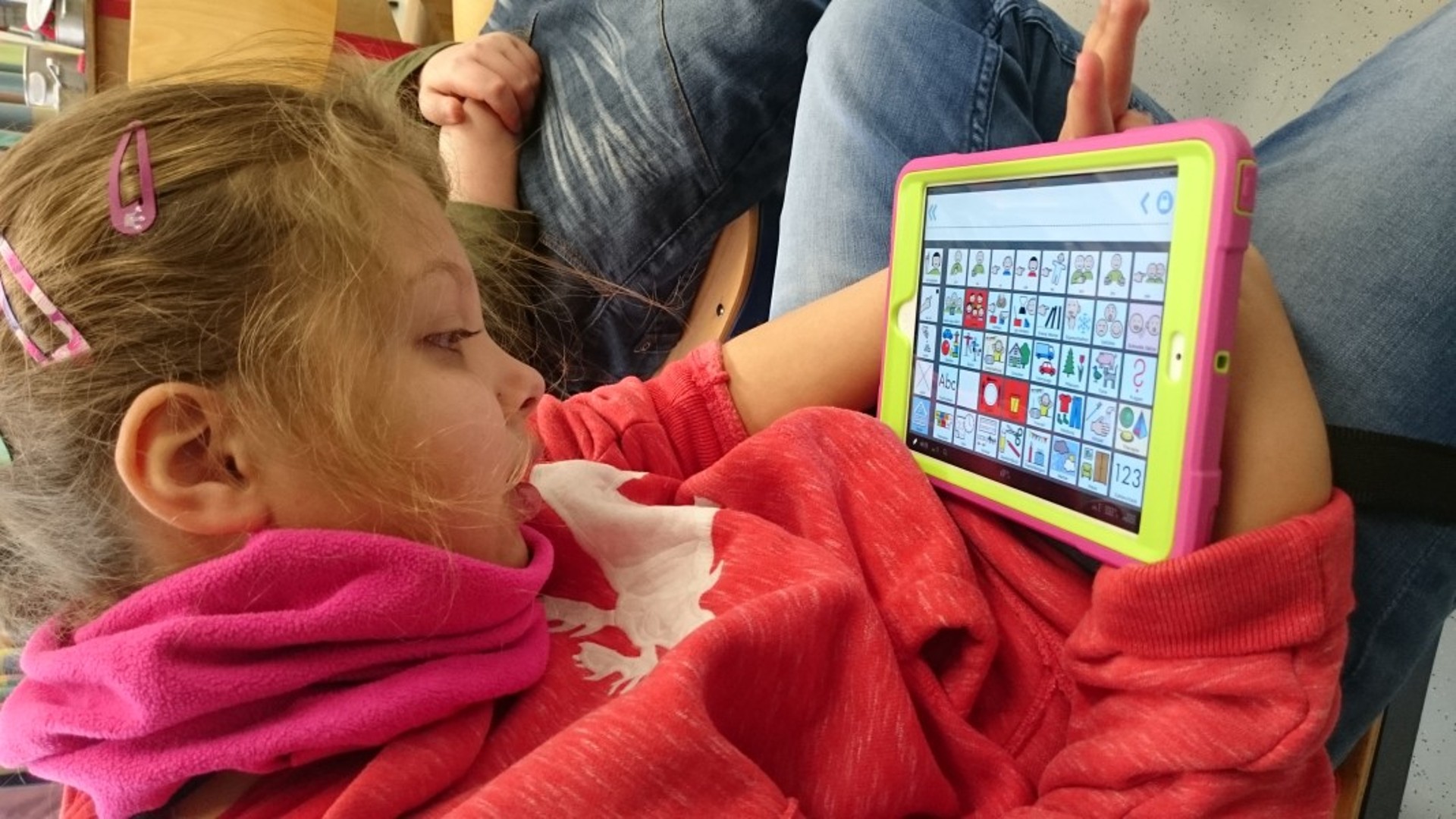 Ein Mädchen hält ein IPadin den Händen. Auf dem Bildschirm sind Metacom-Symbole zu sehen.